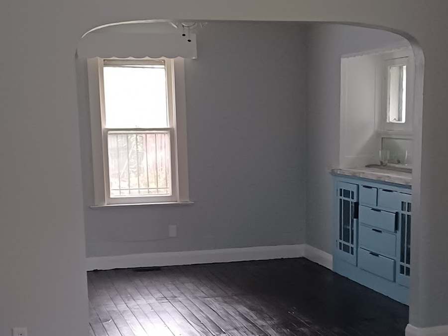 The same room finished: light gray walls, dark refinished floors, a bright window and the built-in cabinet painted light blue.